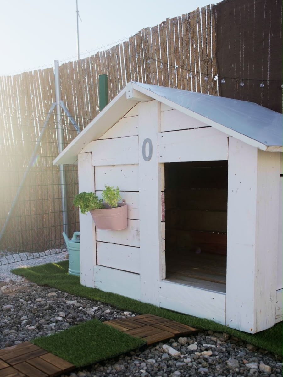 Caseta de madera pintada de blanco sobre césped, junto a la valla de cañizo.