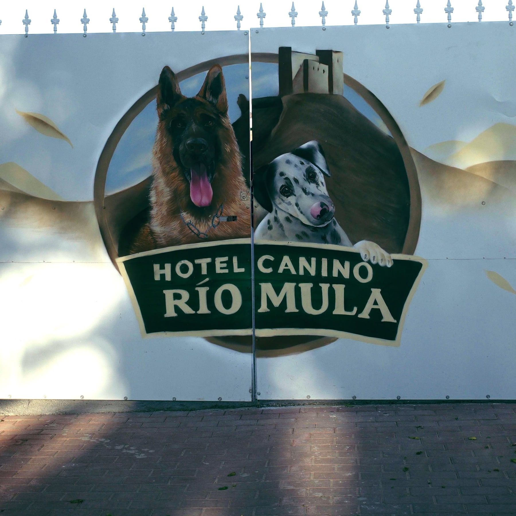 Portón metálico blanco con un mural pintado a mano: dos perros, un castillo y el rótulo Hotel Canino Río Mula.